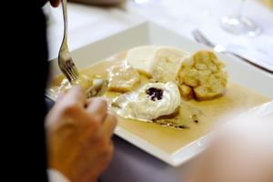 Person schneidet in einen Dessertteller mit Vanillesauce, Eis mit Beerentopping und Gebäck im Hotel Ludmila in Mělník.