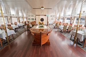 Elegantes Schiffsrestaurant auf der MS Florentina mit bootsförmigem Buffettisch aus Holz, weiß gedeckten Tischen und großen Fenstern.