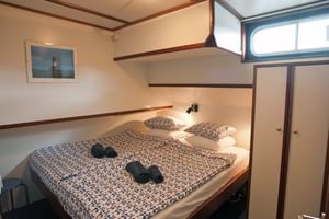 Compact ship cabin on MS Sarah with double bed, patterned bedding, porthole window, built-in storage, and wooden trim throughout.