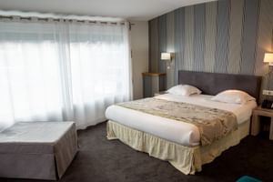 Modernes Hotelzimmer im Grand Hotel Toulouse mit Doppelbett, grauem Kopfteil, gestreifter Tapete, Nachttischlampen und Einzelbett am Fenster.