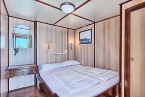Innenraum der San Snova 2-Bett-Kabine mit Doppelbett, weißer Bettwäsche, Holzvertäfelung, Spiegel, Leselampen und Schiffskunst an den Wänden.