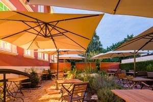 Außenterrasse im Parkhotel Jever mit gelben Sonnenschirmen, Holztischen und Stühlen, umgeben von Pflanzen und orangefarbenen Wänden unter Abendhimmel.