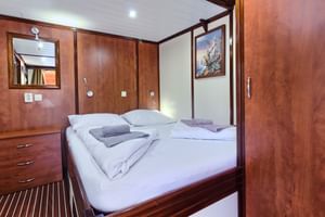 Innenraum der Andela Lora 2-Bett-Kabine mit weißer Bettwäsche, Holzverkleidung, Spiegel, Kunstwerk und eingebauten Schubladen.