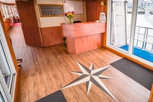 Empfangsbereich der MS Fluvius mit Holztheke, Kompassrosen-Intarsie im Boden und Glastüren zum Außendeck mit Hafenblick.