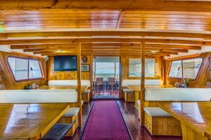 Innenraum des Linda Schiff Salons mit Holzwänden, weißen Polstersitzen, Esstischen und großen Fenstern mit Meerblick.