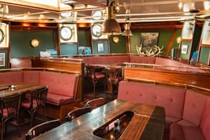 Innenraum des Antigua-Schiffsrestaurants mit geschwungenen roten Bänken, Holztischen, grünen Wänden, Bullaugen und Geweih-Dekoration.