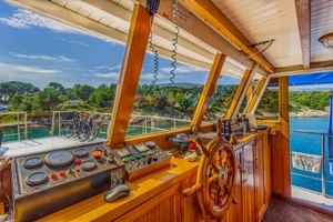 Innenraum des Steuerhauses der Linda mit hölzernem Steuerrad, Kontrollpanel mit Anzeigen und Panoramafenstern mit Blick auf Küstengewässer.