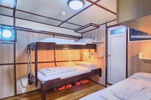 Moderne Dreibettkabine mit Etagenbett und Einzelbett, Holzverkleidung, Leselampen und Kleiderschrank auf Schiff San Snova.