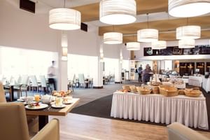 Moderner Frühstücksraum im Upstalsboom Varel mit Buffettischen, weißen Pendelleuchten, beiger Bestuhlung und hellem Essbereich mit großen Fenstern.