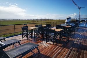 Sun deck of MS Magnifique IV with wooden flooring, black metal tables and chairs, safety railings overlooking green countryside fields.
