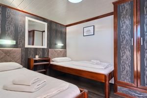 Zweibettkabine auf MY Magellan mit zwei Betten, Holzschrank, Spiegel, Wandlampen und gemusterten Wandpaneelen. Weiße Handtücher auf Betten.