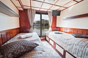 Zweibettkabine auf der MS Florentina mit Holzverkleidung, dekorativen Deckenbalken und Fenster mit Blick auf Kanal und historische Gebäude.