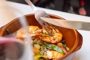 Terrakotta-Schale mit gegrillten Garnelen und Gemüse, serviert mit Gabel und Messer im Restaurant des Grand Hotel Toulouse.