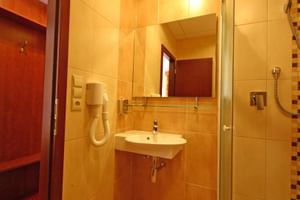 Modernes Badezimmer mit gelben Fliesen, Wandwaschbecken, Spiegel, Glasdusche mit Mosaikfliesen und Haartrockner im Hotel Ludmila in Mělník.