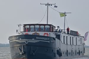 MS Magnifique IV Flusskreuzfahrtschiff auf offenem Wasser. Das Schiff hat einen dunklen Rumpf und weißen Aufbau mit großen Fenstern.