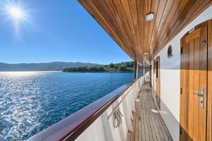 Holzdeck des Kreuzfahrtschiffs MY Magellan mit weißen Geländern und Kabinentüren, mit Blick auf blaue Adria und kroatische Küste.