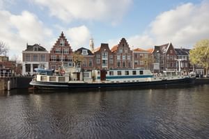 MS Flora, a white and green passenger vessel, moored along a canal with traditional Dutch gabled houses and a church tower in the background.
