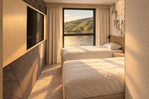 Modern twin cabin on MS Veloria with two beds, wooden paneling, wall-mounted TV, and large window showing river and hillside landscape.