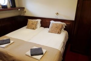 Kompakte Schiffskabine mit zwei Einzelbetten, weißer Bettwäsche, Zierkissen und dunkler Holzvertäfelung auf SIMMER FAN FRYSLÂN.