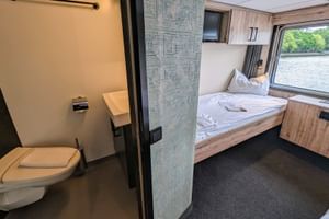 Zwei-Bett-Kabine auf dem Oberdeck der MS Princess mit Bad. Weißes Bett, Holzverkleidung, Fenster mit Flussblick und angrenzende Toilette sichtbar.
