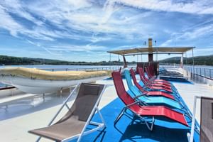 Sun deck of ship MY Andela Lora with rows of blue and red loungers, life raft, and covered seating area. Croatian coastline visible in background.