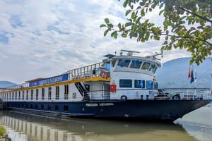 Flusskreuzfahrtschiff MS Prinzessin Katharina in Untermühl, Österreich. Das weiß-blaue Schiff liegt vor grünen Hügeln unter bewölktem Himmel.