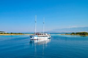 Weiße Motoryacht MS Aria mit zwei Masten vor Anker in ruhigen blauen Gewässern vor der kroatischen Küste mit grünen Inseln und Bergen.