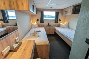 Zweibettkabine auf der MS Princess mit drei Einzelbetten, holzgetäfelten Wänden, Fenstern mit Vorhängen, Leselampen und einem Schreibtisch.