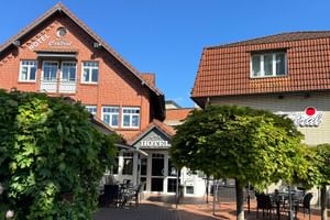 Hotel Central in Zeven mit roter Backsteinfassade und Außenterrasse. Zwei Gebäude flankieren einen Innenhof mit grünen Bäumen und Sitzbereich.