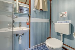 Kompaktes Badezimmer auf Schiff San Snova mit weißem Waschbecken, Toilette, Dusche und blau gestreiften Wänden.
