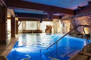 Hallenbad mit Steinmauer-Wasserfall, Holzbalken und Dämmerungshimmel-Decke im Upstalsboom Hotel Varel Spa in Ostfriesland.
