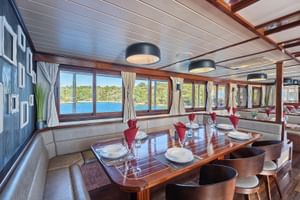 Innenraum des MY Magellan Restaurants mit polierten Holztischen, beiger Bestuhlung und großen Fenstern mit Blick auf die kroatische Küste.