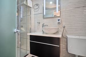 Modernes Badezimmer auf MY Magellan mit Glasdusche, weißem Waschbecken auf dunklem Unterschrank, strukturierten Wandfliesen und WC.