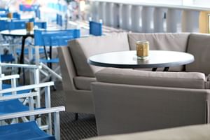 Moderner Loungebereich auf dem Sonnendeck der MS Normandie mit grauen Sofas um weiße Tische und blauen Liegestühlen im Hintergrund.