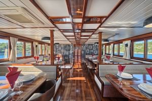 Innenraum des Magellan Schiff-Salons mit Holz-Esstischen, roten Servietten, Panoramafenstern, sichtbaren Deckenbalken und nautischem Dekor.