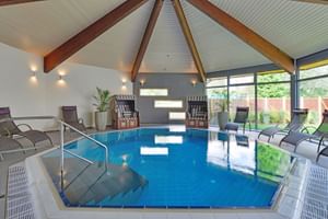 Hallenbad im Landhotel Schnuck mit gewölbter Holzdecke, Liegestühlen, Strandkörben und großen Fenstern mit Blick auf den Garten.