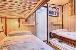 Holzkabine auf Schiff San Snova mit zwei Betten, weißer Tür, Leselampen und gerahmtem Foto. Holzverkleidung und Balkendecke sichtbar.