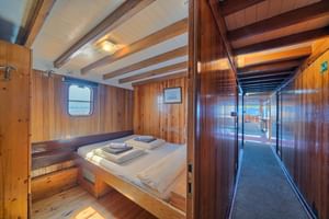 Holzkabine mit Doppelbett, sichtbaren Deckenbalken, Bullauge und Gangblick. Weiße Bettwäsche mit gefalteten Handtüchern auf der Linda.