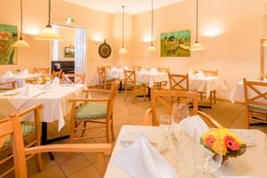 Helles Restaurant mit Holzstühlen, weißen Tischdecken, Pendelleuchten und bunten Gemälden an cremefarbenen Wänden im Hotel Geheimer Rat.