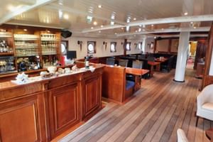 Innenraum des Restaurants der SIMMER FAN FRYSLÂN mit Holzboden, Bartheke, Esstischen, Stühlen und runden Bullaugen an den Wänden.