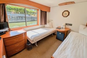 2-Bett-Kabine auf MS Olympia mit zwei Betten, großem Fenster mit Flussblick, Holzmöbeln, TV und beigem Teppich.