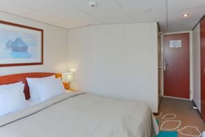 Helle Kabine auf der SE Manon mit Doppelbett, weißer Bettwäsche, grauer Tagesdecke, Holzkopfteil, Nachttischlampe, gerahmtem Bild und Schrank.