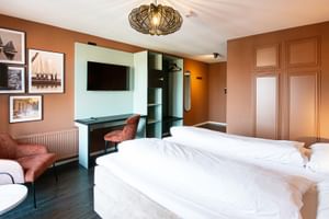 Modernes Hotelzimmer mit zwei Einzelbetten, terrakottafarbenen Wänden, maritimer Kunst, Flachbildfernseher und rostfarbenen Sesseln im Hotel Old Dutch Volendam.