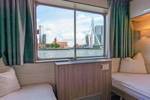 2-Bett-Kabine auf dem Oberdeck der MS Normandie mit zwei Einzelbetten, großem Fenster mit Blick auf die Rotterdamer Skyline mit Erasmusbrücke.