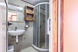 Kompaktes Badezimmer auf der Andela Lora mit weißem Waschbecken, gebogener Glasduschkabine, Spiegel und Holzschrank über dem Waschbecken.