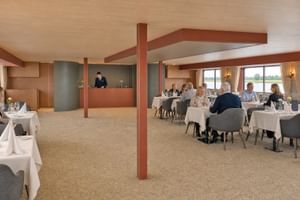 Spacious restaurant aboard MS Veloria with white-clothed tables, gray upholstered chairs, and large windows overlooking the river landscape.