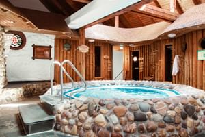 Innen-Spa-Pool mit Steinumrandung im Upstalsboom Hotel Varel. Holzwände, sichtbare Balken und Saunatüren im Hintergrund.