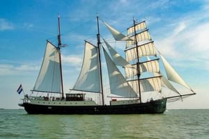 Traditionelles dreimastiges Segelschiff Simmer Fan Fryslân mit weißen Segeln auf ruhigem Wasser unter blauem Himmel mit Wolken.
