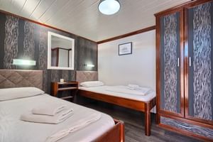 Moderne Magellan Schiffskabine mit zwei Einzelbetten, Holzmöbeln, gemusterter Tapete, Einbauschrank und nautischer Kunst an weißen Wänden.