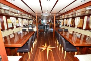 Innenraum des Andela Lora Schiffssalons mit polierten Holzböden mit Kompassrose-Einlage, Esstischen mit schwarzen Stühlen und Fenstern.